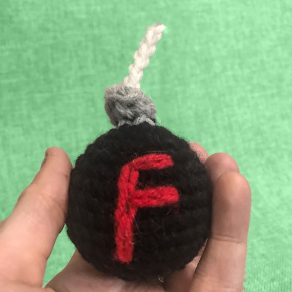A hand-crocheted F-bomb (literally a tiny bomb with the letter F) — the cleverest possible way to drop profanity on someone's desk without actually saying it.