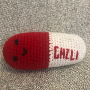 May include: A red and white crocheted pill-shaped plush toy with a smiling face and the word "CHILL" embroidered on the white side.