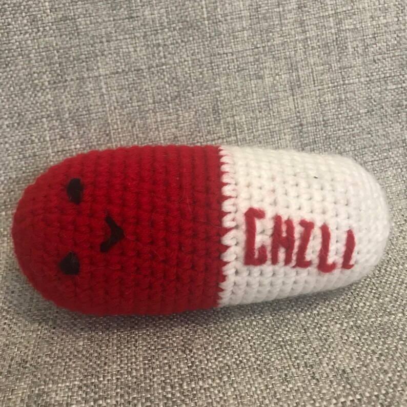 May include: A red and white crocheted pill-shaped plush toy with a smiling face and the word "CHILL" embroidered on the white side.