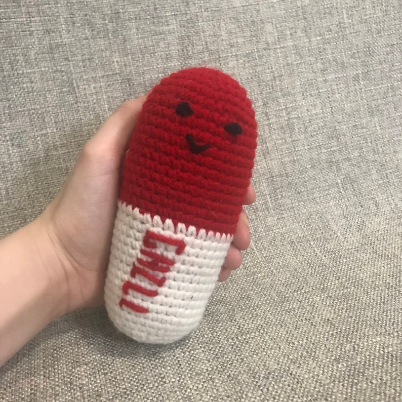 May include: A crocheted red and white pill-shaped plush toy with a smiling face and the word "CRAZY" written on the white part.