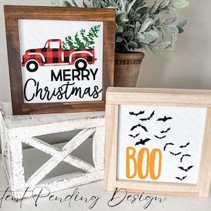 May include: Two wooden framed signs, one with a red and black plaid truck with a Christmas tree and the text "Merry Christmas", and the other with black bats and the text "BOO" in orange.