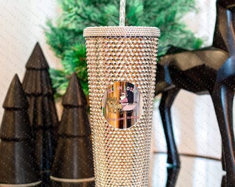 May include: A silver glitter tumbler with a round sticker that says "Get in Loser, We're Going Sledding" with a cartoon image of Santa Claus on a sled.
