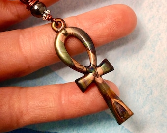 May include: A copper and black necklace with an iridescent green and brown ankh pendant.