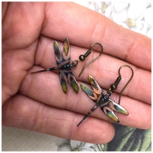 May include: A pair of dragonfly earrings with a bronze finish. The dragonflies have a multi-colored design with shades of blue, green, and pink.