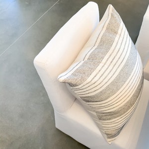 May include: A white chair with a black and white striped pillow. The chair is upholstered in a soft, white fabric.