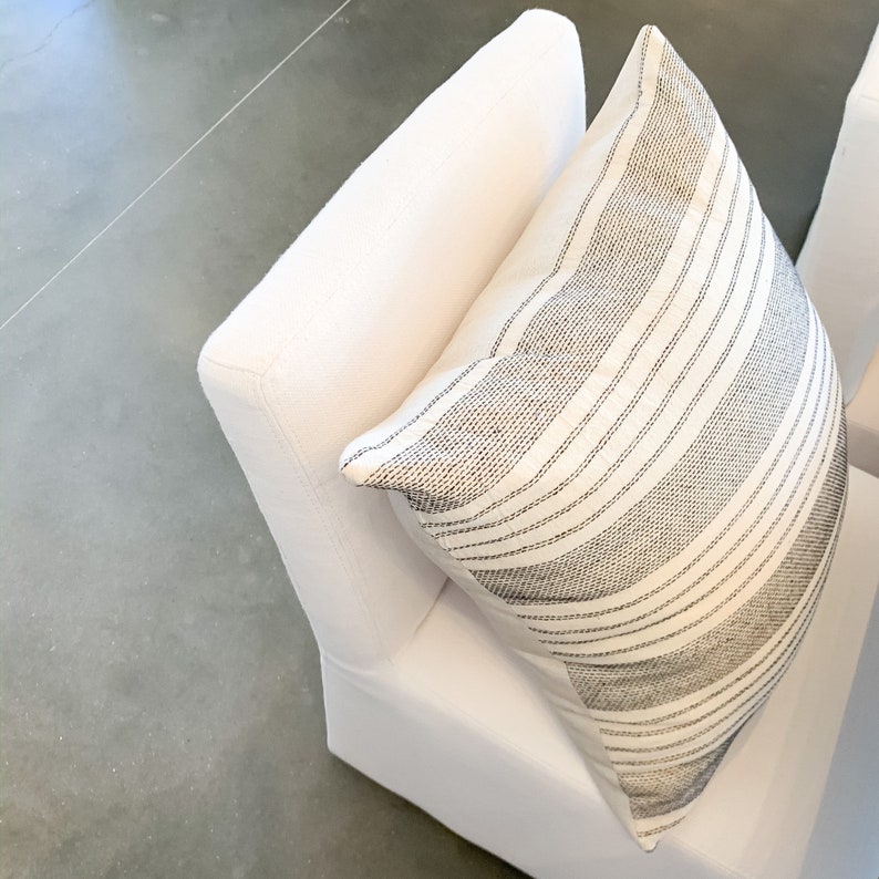 May include: A white chair with a black and white striped pillow. The chair is upholstered in a soft, white fabric.