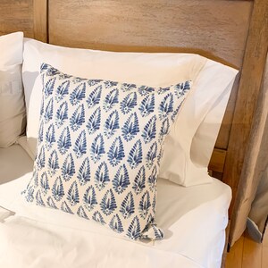 K&ouml;nnte beinhalten: Ein wei&szlig;es Kissen mit einem blauen und wei&szlig;en gemusterten Kissen darauf. Das Muster ist ein sich wiederholendes Design aus blauen Tropfenformen mit wei&szlig;en Akzenten.