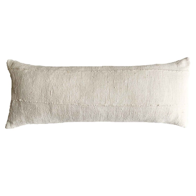 May include: A long, rectangular off-white lumbar pillow. The pillow has a textured, woven appearance with horizontal seams. The neutral color and simple design suggest a rustic or bohemian style, suitable for a bed or sofa.