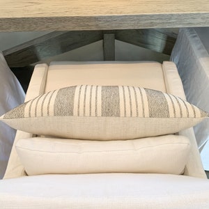 May include: A white couch with two white pillows and a black and white striped pillow on top.