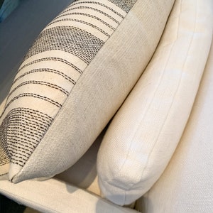 May include: Two white throw pillows with a striped pattern on one pillow. The pillows are made of a soft, textured fabric.
