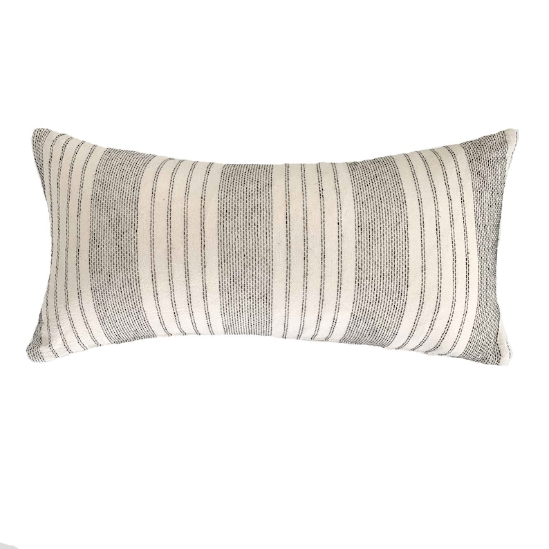 May include: A long, rectangular pillow with a white background and thin black stripes. The pillow is made of a soft, woven fabric.