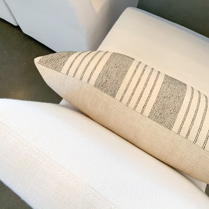 May include: A white throw pillow with black stripes. The pillow is made of a soft, natural fabric and has a subtle texture.