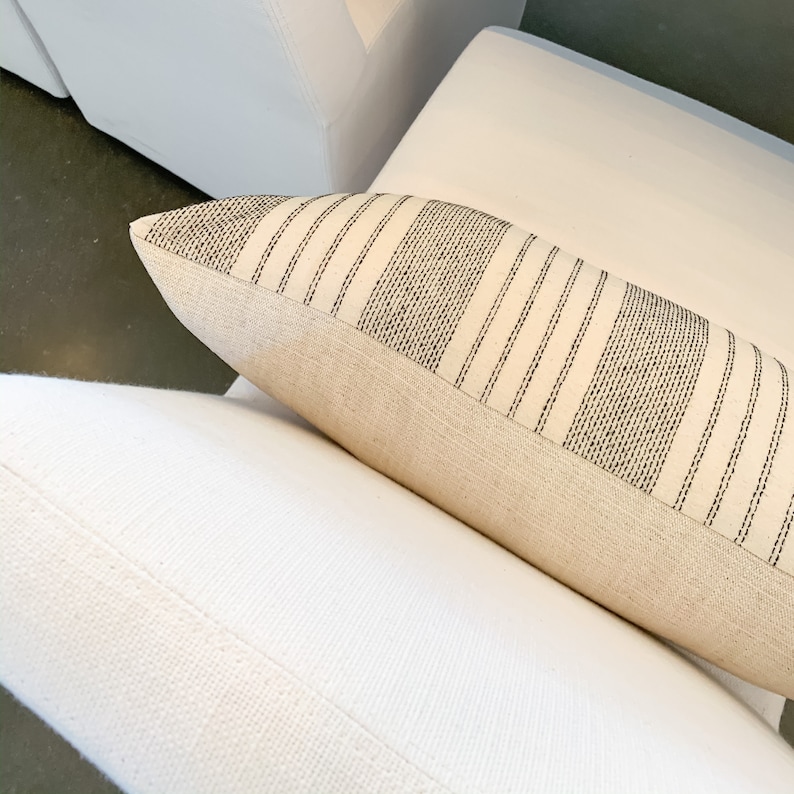 May include: A white throw pillow with black stripes. The pillow is made of a soft, natural fabric and has a subtle texture.
