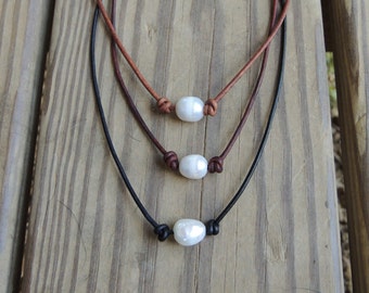May include: Three leather necklaces with a single pearl pendant on each. The necklaces are brown, black, and brown. The pearls are white.