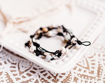 May include: A multi-strand bracelet with black cord and various colored beads, including white, blue, and green, on a white plate.