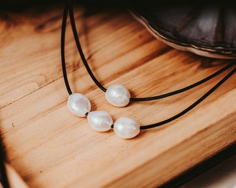 May include: A simple necklace with a black leather cord and four white pearl beads.