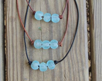 May include: Two leather necklaces with light blue glass beads. The necklaces are on a wooden surface.