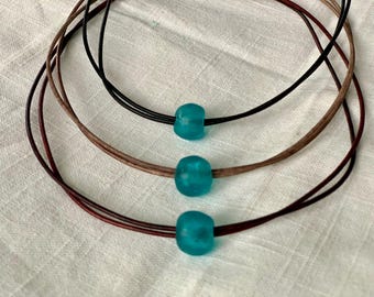 May include: Three leather necklaces with turquoise blue glass beads. The necklaces are layered on top of each other.
