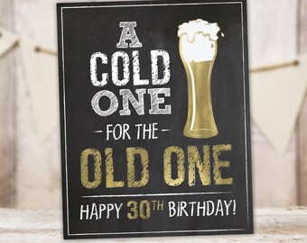 Può includere: Un cartello nero in ardesia con lettere dorate che recita "A Cold One For The Old One Happy 30th Birthday!" con un'illustrazione di un bicchiere di birra dorato.