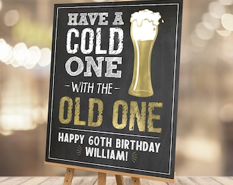 Può includere: Un cartello nero in stile lavagna su un cavalletto di legno. Il cartello recita "Have a Cold One with the Old One" con una grafica di un bicchiere di birra dorato. C'è anche scritto "Happy 60th Birthday William!" in lettere bianche e oro. Il cartello misura 40,6 x 50,8 cm.
