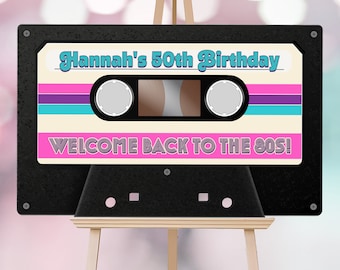 May include: A black cassette tape with a pink, purple, and blue design. The text "Hannah's 50th Birthday" and "Welcome Back to the 80s!" is printed on the tape. The tape is 36 inches by 24 inches and 24 inches by 18 inches.
