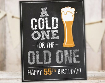 Può includere: Un cartello nero in ardesia con testo bianco che recita "A Cold One - For The Old One Happy 55th Birthday!" Un bicchiere di birra con la schiuma bianca è illustrato sul cartello.