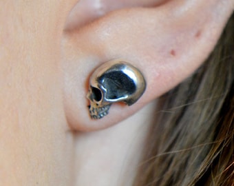May include: A pair of silver skull stud earrings. The earrings are small and delicate, and they are perfect for adding a touch of edgy style to any outfit.