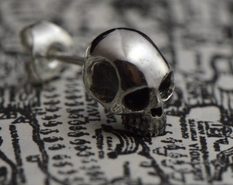 May include: A pair of silver skull stud earrings. The earrings are small and detailed, with a realistic skull design.