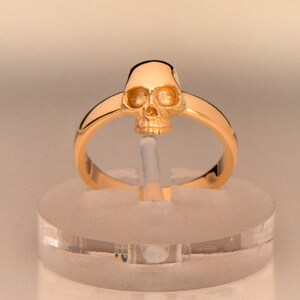 May include: A gold ring with a detailed skull design. The skull is raised and has a three-dimensional appearance.