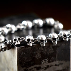 May include: A silver bracelet with a chain made of small skull charms.