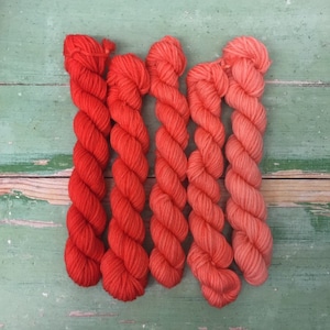 Könnte beinhalten: Fünf Knäuel Garn in Rot- und Orangetönen. Das Garn ist in einem Farbverlauf von Dunkelrot bis Hellorange angeordnet.
