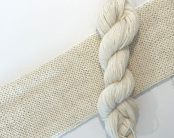 May include: A skein of off-white yarn next to a swatch of knitted fabric in the same color.