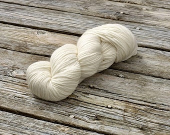 May include: A skein of white yarn, wound into a loose coil, sits on a weathered wooden surface.