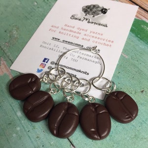 May include: Set of six brown coffee bean stitch markers with silver rings. The stitch markers are attached to a card with the text "Ewe Momma Hand dyed yarns and handmade accessories for knitting and crochet www.ewemomma.com.uk Unit 12, The Suttermarket Enniskillen Co Fermanagh, B74 7DU @evemommaknits @emma malnits"