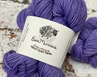 May include: Two skeins of purple hand-dyed yarn with a white label that reads "Ewe Momma Colorlicious Hand Dyed Yarns".