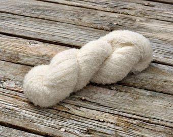 May include: A skein of soft, white yarn, with a fluffy texture, is displayed on a weathered wooden surface.