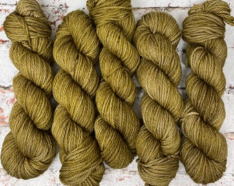 May include: Close-up of five skeins of olive green yarn. The yarn is thick and twisted, with a slightly textured appearance. The skeins are arranged in a row, with the ends of the yarn visible. The color is a muted, earthy green.