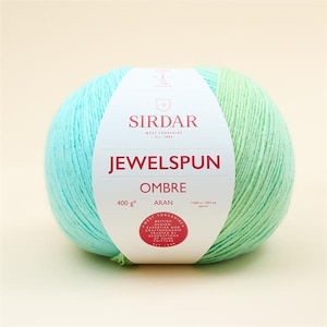 Puede incluir: Un ovillo de lana Sirdar Jewelspun Ombre Aran en un degradado de color azul claro y verde. La etiqueta dice "Sirdar Jewelspun Ombre Aran 400g".