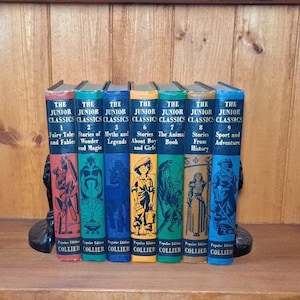 May include: A collection of vintage children's books, titled "The Junior Classics," displayed on a wooden shelf. The books have colorful spines with titles like "Fairy Tales" and "Stories from History." They are held by decorative bookends.