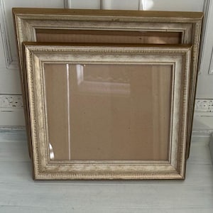 May include: Two square picture frames with a distressed gold and white finish. The frames feature a decorative beaded inner edge and a smooth outer border. Each frame has a clear glass front and a plain brown backing board visible inside.