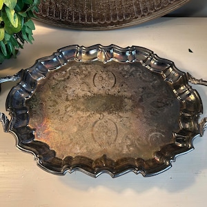 May include: A silver serving tray with ornate edges and two handles. The tray has a decorative, embossed pattern.
