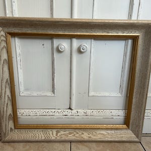 May include: A rectangular picture frame featuring a wide, light-coloured wood grain border with a prominent, textured pattern. The inner edge of the frame is accented with a thin, smooth, metallic gold trim that creates a distinct contrast.