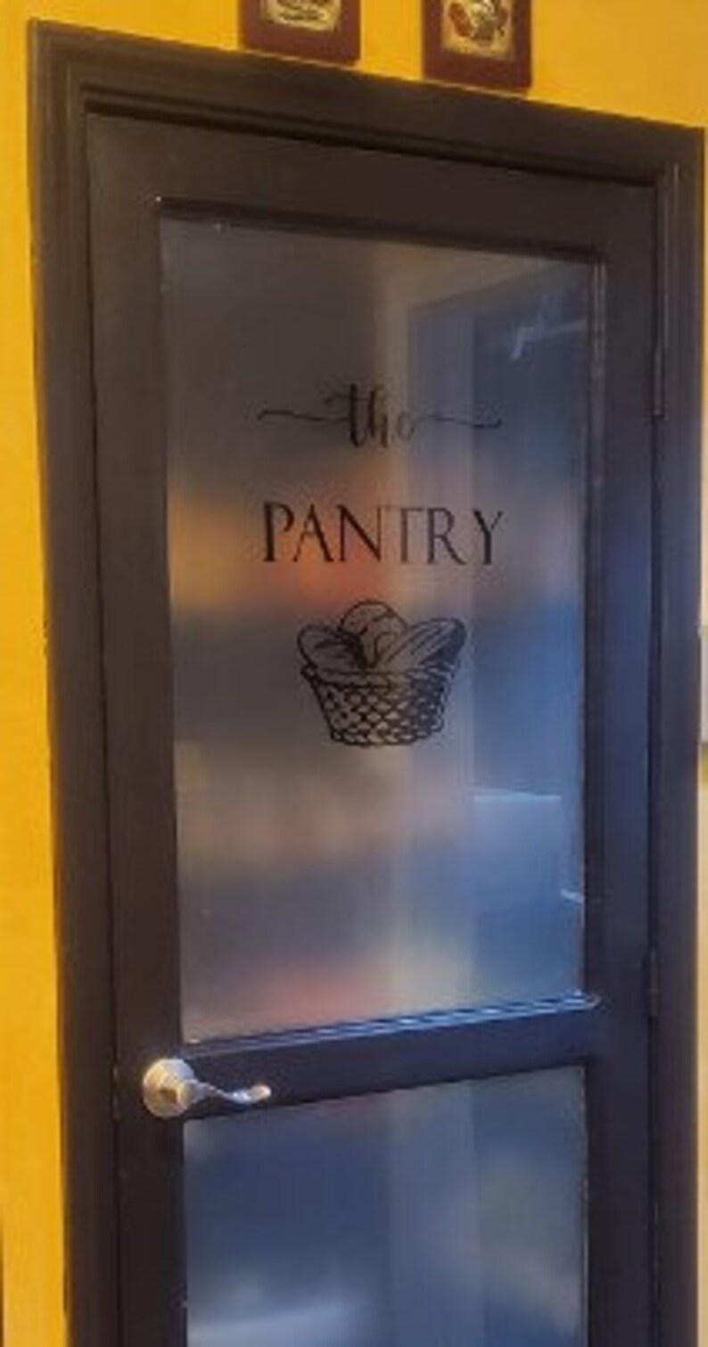 Op de afbeelding: Een zwarte deur met een matglas paneel. Het glas heeft een zwarte vinyl sticker met de tekst "the pantry" en daaronder een mand met brood.