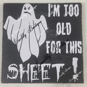 May include: A black wooden sign with white text and a white ghost graphic. The text reads "I'm too old for this sheet!"