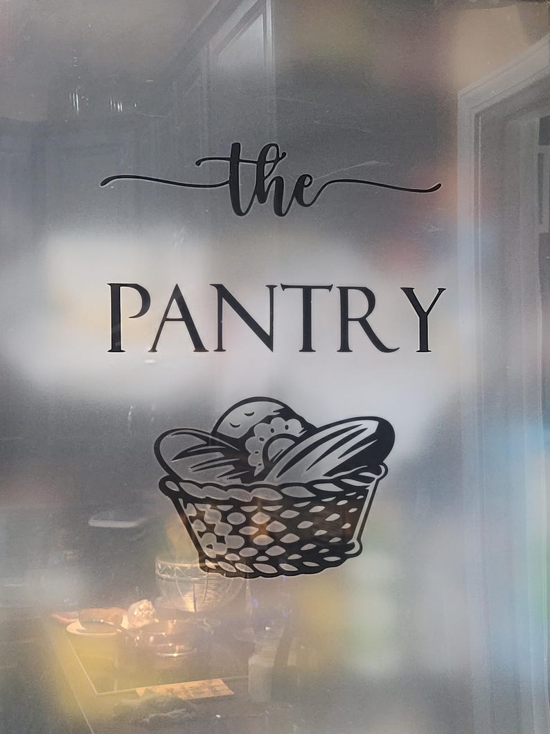 Op de afbeelding: Een matglazen deur met een zwarte vinyl sticker waarop "the PANTRY" staat, met daaronder een gestileerde broodmand.