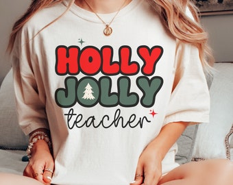 May include: A white long-sleeved shirt with the text "HOLLY JOLLY teacher" in red, green, and white. The shirt has a retro design with a Christmas tree graphic.