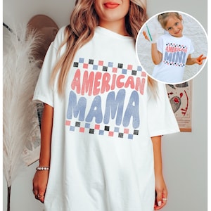 May include: White oversized t-shirt with the text "AMERICAN MAMA" in pink, blue, and black lettering with a checkered pattern.