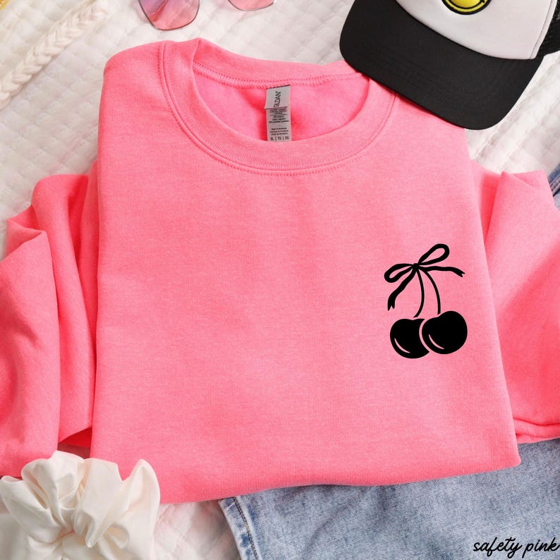 May include: A pink sweatshirt with a black cherry design on the front. The cherries have a black bow on top.