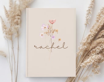May include: A beige journal with a watercolor illustration of a bouquet of pink and peach flowers. The name "rachel" is written in brown cursive script below the flowers.