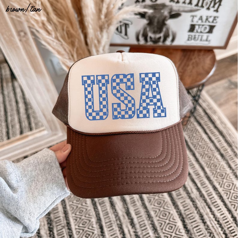 May include: A white and brown trucker hat with a blue and white checkered "USA" graphic.
